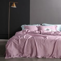 a bed with pink sheets and pillows in a room next to a lamp on the floor