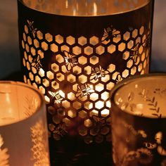 three lit candles sitting next to each other in front of a metal container with honeycombs on it