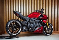 a red and black motorcycle parked in front of a wooden paneled wall on wheels