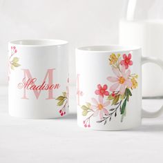 two coffee mugs with floral designs on them, one is white and the other is pink