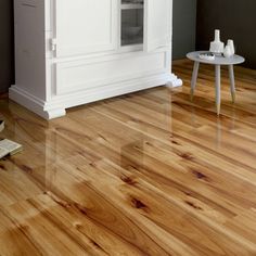 a kitchen with white cabinets and wood flooring in the middle, next to a small table