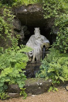 a statue is sitting in the middle of some plants and trees, with water coming out of it