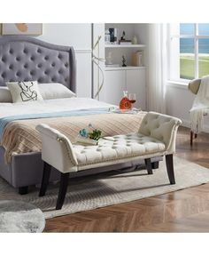 a bed with a tufted upholstered headboard and footstool in front of a window