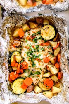 two foil packets filled with food on top of a table next to another bag full of potatoes, carrots and zucchini