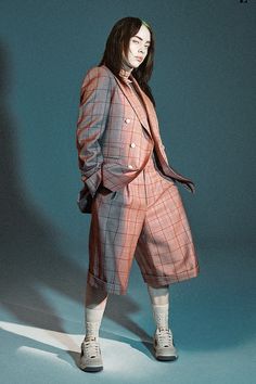 a woman standing in front of a blue background wearing an orange plaid suit and white socks