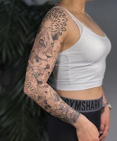 a woman with a tattoo on her arm and chest is standing in front of a plant