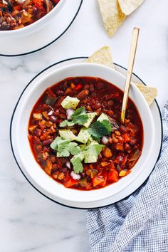 two bowls of chili with tortilla chips on the side