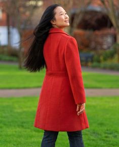 a woman in a red coat is standing on the grass and looking up at the sky