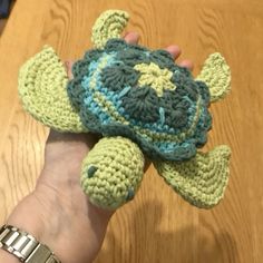 a hand holding a crocheted turtle on top of a wooden table next to a person's arm