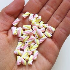 a hand is full of candy canes with pink and yellow stripes on them as if they were made out of marshmallows