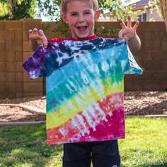 a young boy standing in the grass with his hands up and wearing a tie - dyed shirt