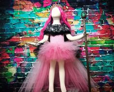 a mannequin dressed in pink, black and white clothes with a cane standing next to a brick wall