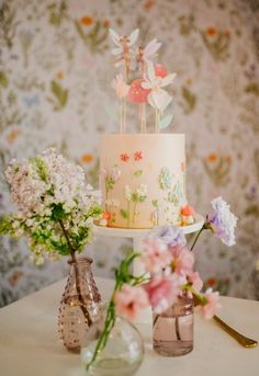 two vases with flowers are sitting on a table next to a cake and knife