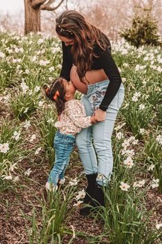 a mother and her toddler girl in a field of daisies with trees in the background