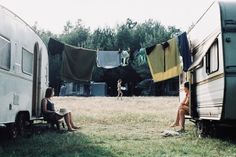 two women sitting on the ground next to an rv and some clothes hanging out to dry