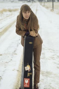 a woman is standing in the snow with her skateboard on it's back