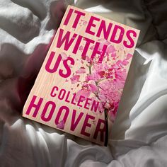 a pink book sitting on top of a white bed covered in sheets and pillows with the title it ends with us