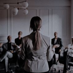 a woman standing in front of a group of people with her back to the camera