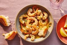 a bowl filled with shrimp next to slices of lemon and bread on top of a table