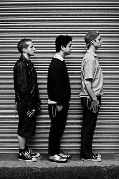 three young men standing next to each other in front of a garage door with roller shutters