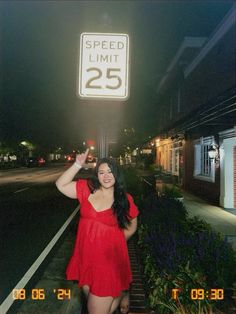 a woman in a red dress is standing under a speed limit sign with her hand up