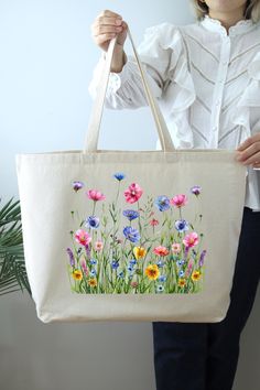 a woman holding a tote bag with flowers painted on it