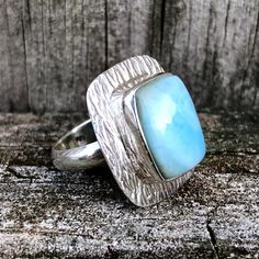 SKU: SS-075Material: 925 stamped sterling silverGemstone(s): Larimar (N)Gemstone Dimensions: 13 X 9 X 2 mmRing Size: US 6Weight: 5.1 gramsThis coastal Larimar ring features a rectangular Larimar cabochon, set with a wavy textured bezel border in a classic comfort ring setting. The wave texture was inspired by ocean waves, and the ring just brings one straight to the beach – crisp salty air, sand in one’s toes and the ocean calling! Silver Larimar Ring Stamped 925, Blue Larimar Round Rings, Elegant Blue Larimar Rings, Unique Silver Larimar Rings, Wave Texture, Blue Larimar Cabochon Rings, Larimar Ring, Larimar Rings, Textured Waves