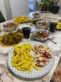 a table full of pasta, salads and other foods on plates with drinks in the background