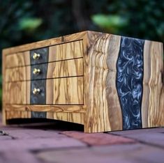 a wooden box with three drawers on it sitting on top of a brick floor next to trees