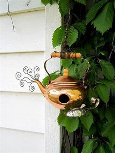 a copper teapot hanging from the side of a house with green leaves around it