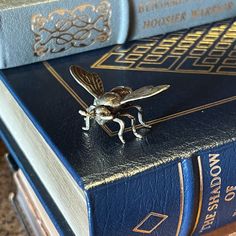 a fly sitting on top of a blue book next to two books with gold trimmings