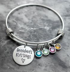 "This personalized grandmother birthstone bracelet includes a silver wire bangle, a 3/4\" disc with \"Grandma's Blessings <3\", or the name of your choice, (example: Grammy, Gigi, Mimi, Nana, Oma, etc), and the swarovski birthstones of your choice. These bangles are perfect to stack together or to wear alone for a simple statement. Bracelet details: The bracelet is adjustable/expandable and is made of stainless steel which will not tarnish or rust like sterling silver, silver plated, or gold Grandma Bracelet, Grandmother Jewelry, Wire Bangles, Personalized Grandma, Birthstone Bracelet, Gift For Grandma, Bangle Bracelets With Charms, Bracelet Online, Hand Stamped Jewelry