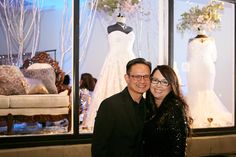 two people standing next to each other in front of a window with dresses on display