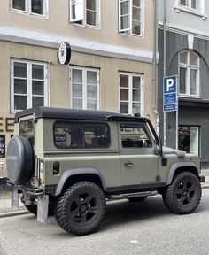 an army green jeep parked on the side of the road in front of a building