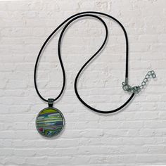 a necklace with a pendant hanging from it's side on a black cord against a white brick wall