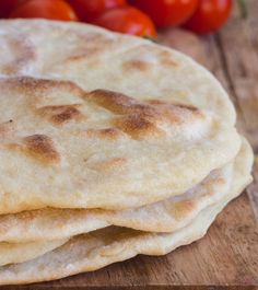 three flat breads sitting on top of a wooden cutting board with tomatoes in the background