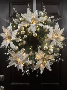 a wreath with white flowers and lights hanging from the front door, on a black door