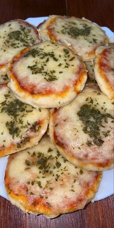 small pizzas with cheese and herbs on a white plate sitting on a wooden table