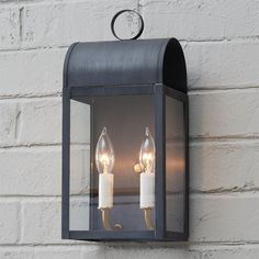 two lit candles are attached to the side of a light fixture on a brick wall