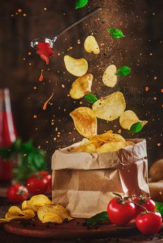 potato chips being tossed into a bag with tomatoes and ketchup on the side