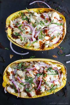 two yellow squash boats filled with chicken, onions and cheese on a black surface next to sliced onion wedges