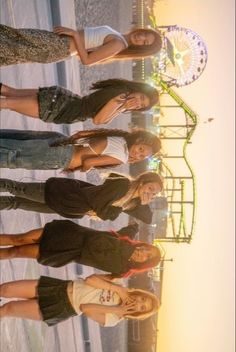 four young women standing next to each other in front of a ferris wheel at an amusement park