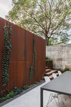 an outdoor dining table and chairs in front of a wall with vines growing on it