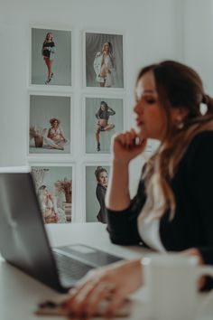 a woman sitting at a table with a laptop computer in front of her and pictures on the wall behind her