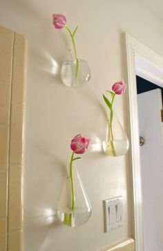 three vases with pink flowers are hanging on the wall next to a light switch