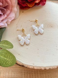 the white butterfly earrings are sitting on top of a piece of wood next to flowers