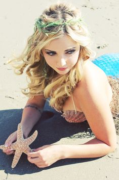 a beautiful young woman laying on top of a sandy beach next to a starfish