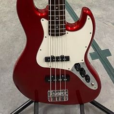 a red and white bass guitar sitting on top of a stand