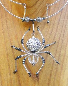 a necklace made out of silver and black beads on a wooden surface with a beaded spider charm hanging from it's back