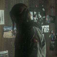 a person with long hair standing in front of a wall covered in pictures and photos